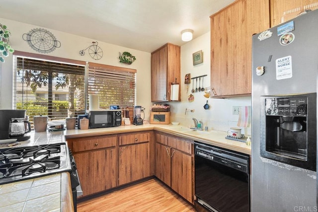 kitchen featuring brown cabinets, tile counters, light wood-style flooring, a sink, and black appliances