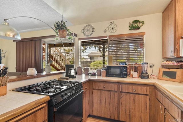 kitchen featuring black appliances, tile counters, brown cabinets, and a sink