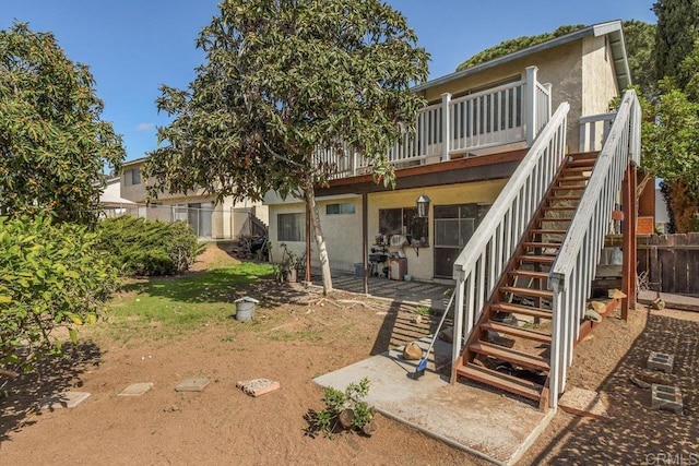 rear view of property with stairs, fence, and stucco siding