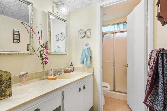 full bath with toilet, a shower stall, a textured ceiling, and vanity