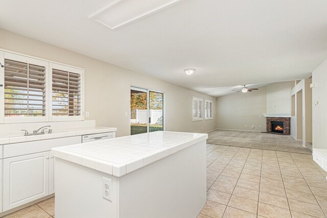 kitchen featuring a brick fireplace, sink, white cabinets, a kitchen island, and tile counters