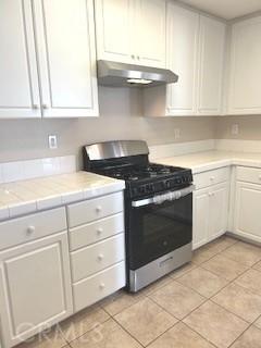 kitchen with tile countertops, light tile patterned floors, white cabinetry, and stainless steel range with gas cooktop