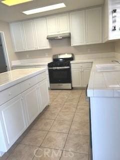 kitchen with light tile patterned floors, white cabinetry, sink, and stainless steel range