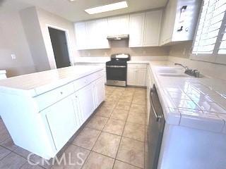 kitchen with white cabinetry, stainless steel appliances, a kitchen island, extractor fan, and light tile patterned floors