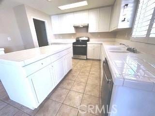 kitchen featuring stainless steel appliances, exhaust hood, light tile patterned floors, white cabinets, and a kitchen island