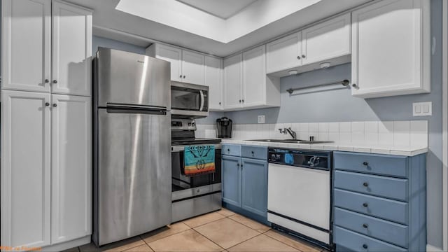 kitchen featuring stainless steel appliances, sink, blue cabinetry, white cabinets, and light tile patterned flooring