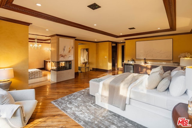 bedroom with hardwood / wood-style floors, a tray ceiling, crown molding, a multi sided fireplace, and a chandelier