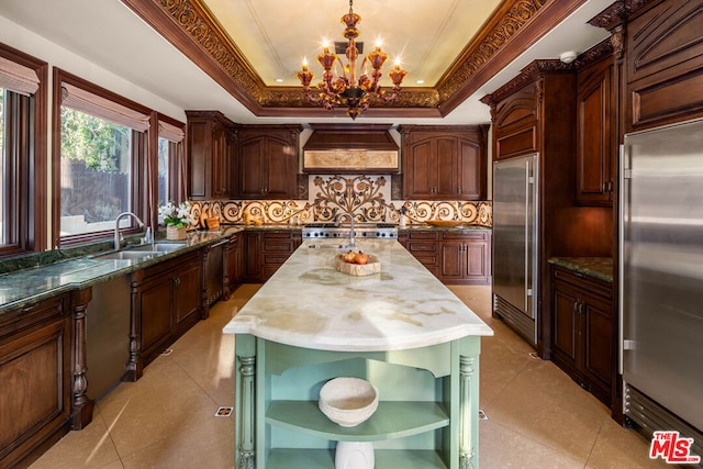 kitchen with custom exhaust hood, decorative light fixtures, stainless steel built in refrigerator, sink, and a tray ceiling