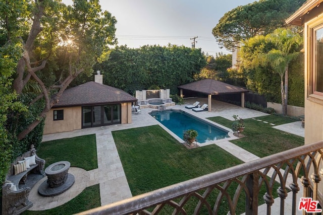 view of swimming pool featuring an outbuilding, a fire pit, an in ground hot tub, a yard, and a patio