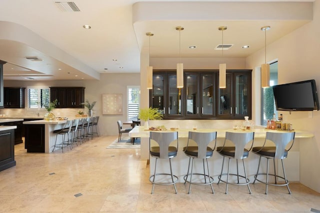 kitchen featuring pendant lighting, dark brown cabinetry, a breakfast bar area, and backsplash