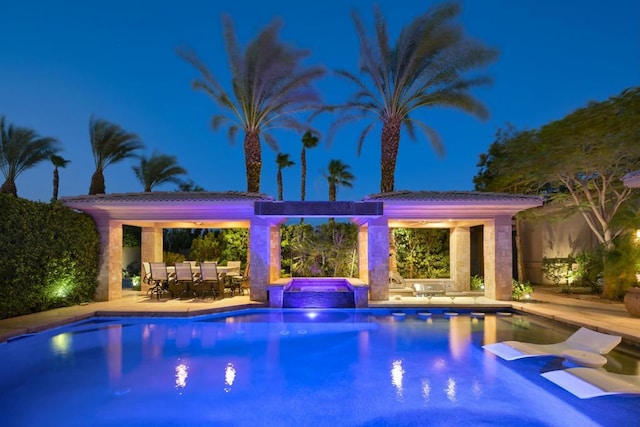 pool at night with a patio area and an in ground hot tub