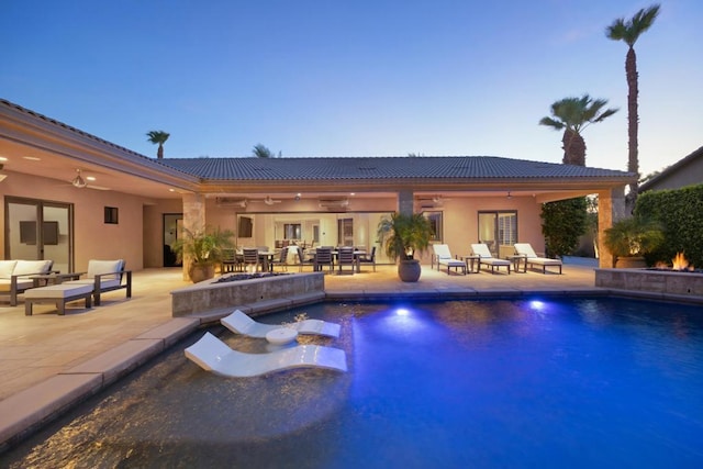 pool at dusk featuring ceiling fan, a patio area, an outdoor hangout area, and a jacuzzi