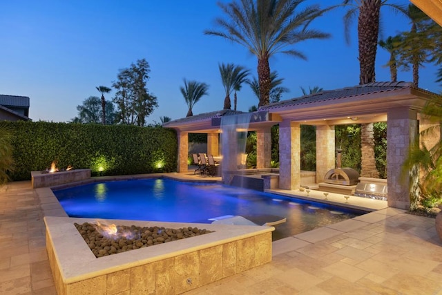 pool at dusk with a patio and exterior kitchen