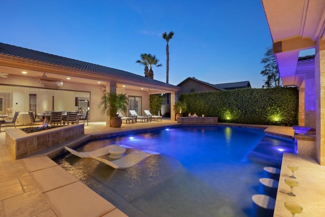 pool at dusk featuring pool water feature and a patio