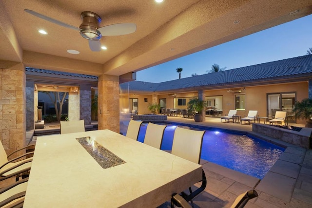 pool at dusk featuring ceiling fan, an outdoor bar, and an outdoor fire pit