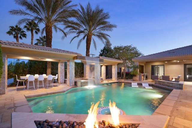 pool at dusk with a fire pit and a patio area