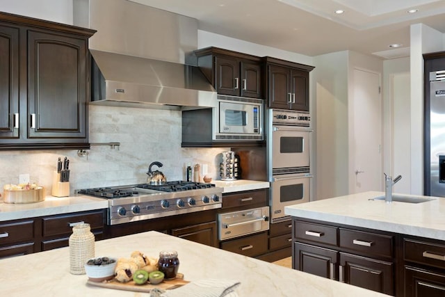 kitchen with decorative backsplash, dark brown cabinetry, wall chimney range hood, and appliances with stainless steel finishes