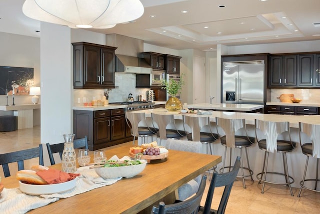 kitchen featuring a tray ceiling, built in appliances, and dark brown cabinetry