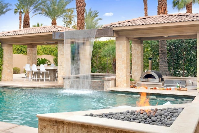 view of swimming pool with a grill, a jacuzzi, pool water feature, area for grilling, and a patio