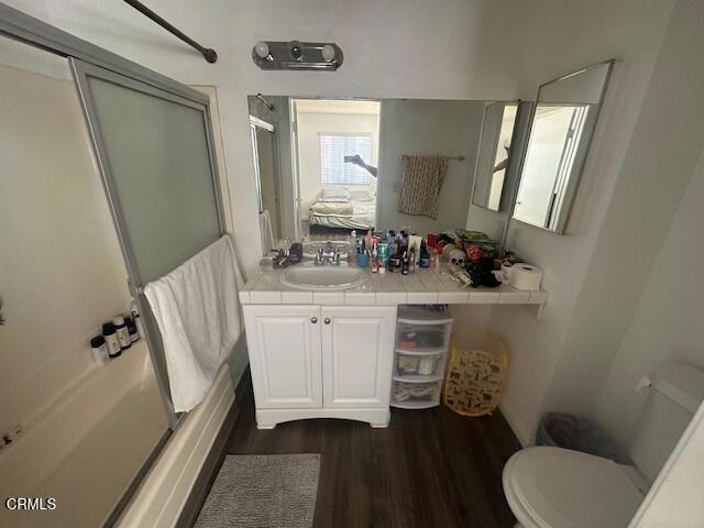 full bathroom featuring toilet, vanity, bath / shower combo with glass door, and hardwood / wood-style flooring