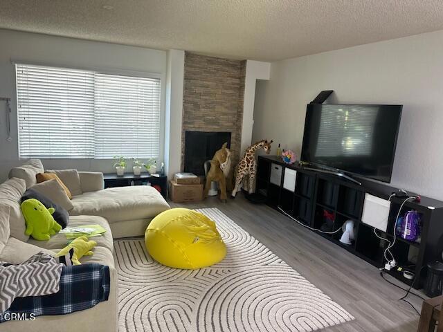 living room with hardwood / wood-style floors, a stone fireplace, and a textured ceiling