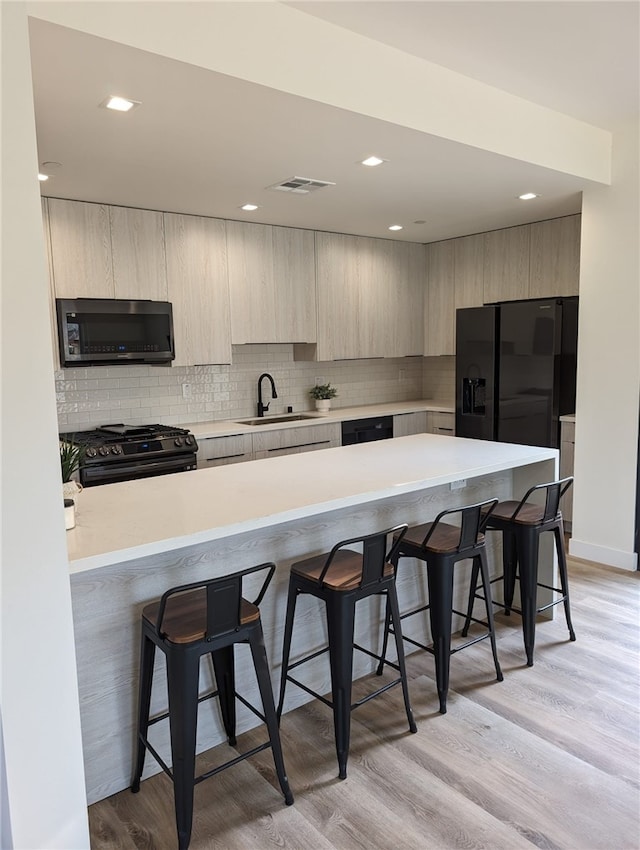 kitchen featuring black appliances, a breakfast bar, light hardwood / wood-style floors, and sink