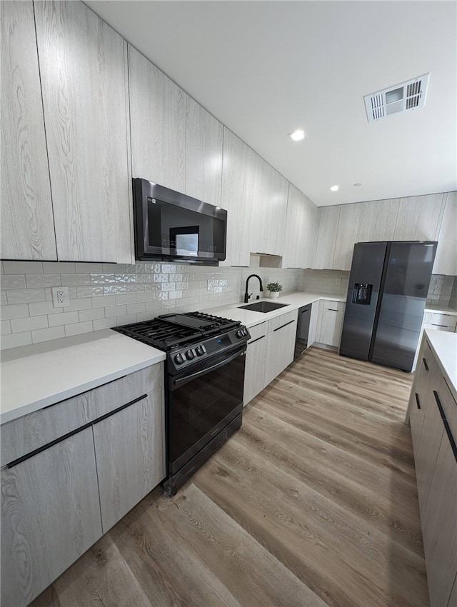 kitchen with sink, light hardwood / wood-style floors, tasteful backsplash, and black appliances