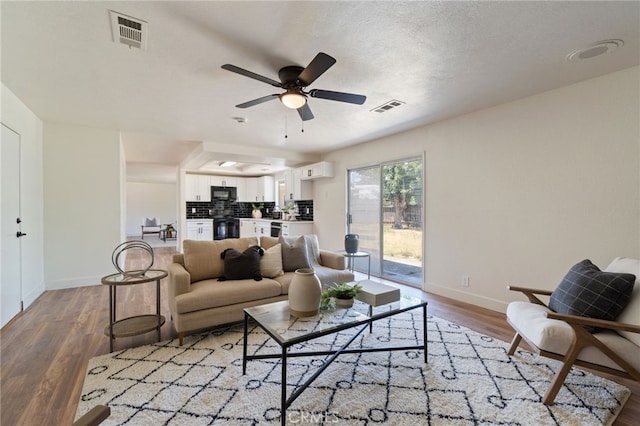 living room with ceiling fan, wood-type flooring, and a textured ceiling