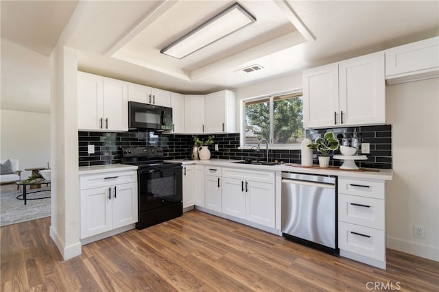 kitchen featuring sink, dark hardwood / wood-style floors, a tray ceiling, white cabinets, and black appliances