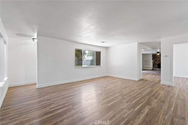 empty room featuring a textured ceiling, a stone fireplace, and dark wood-type flooring