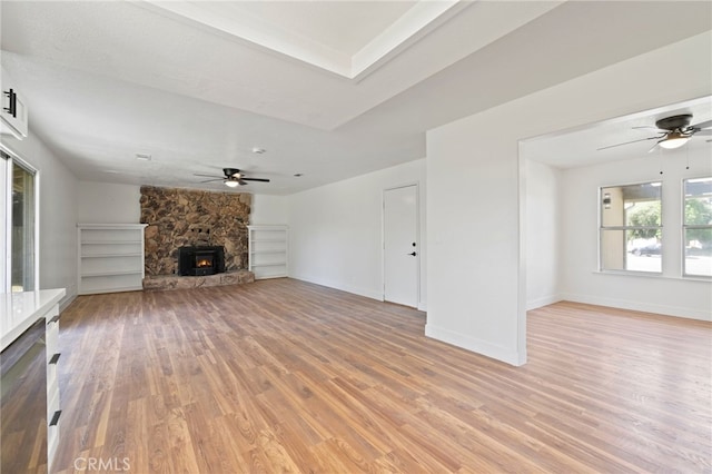 unfurnished living room with a wood stove, ceiling fan, and light wood-type flooring