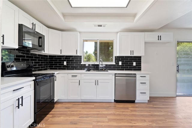 kitchen with black appliances, white cabinetry, sink, and light hardwood / wood-style flooring