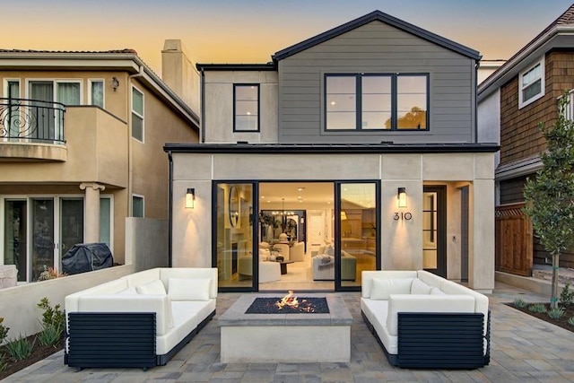 back house at dusk featuring a patio area, a balcony, and an outdoor living space with a fire pit