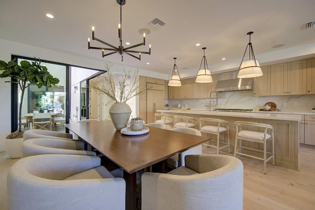 dining space with light hardwood / wood-style floors, sink, and an inviting chandelier