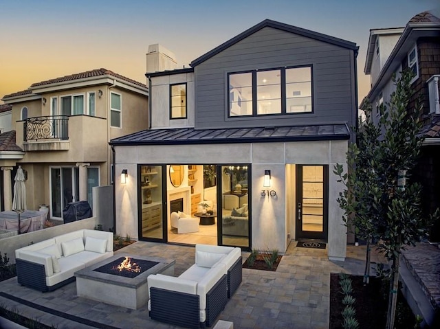 back house at dusk with an outdoor living space with a fire pit, a patio area, and a balcony