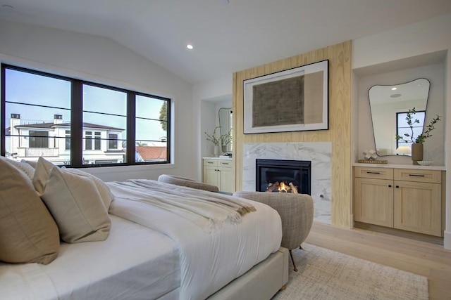 bedroom featuring vaulted ceiling, a high end fireplace, light hardwood / wood-style floors, and ensuite bath