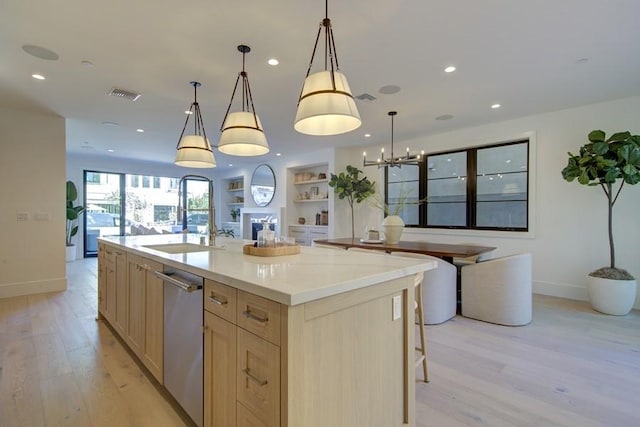 kitchen with decorative light fixtures, dishwasher, a center island with sink, sink, and light brown cabinetry