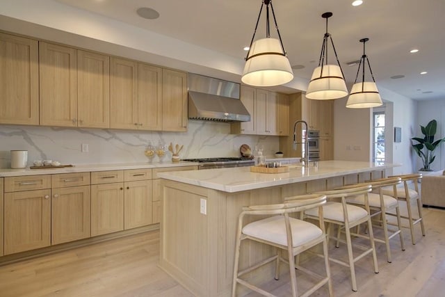 kitchen featuring light brown cabinetry, sink, wall chimney range hood, and an island with sink