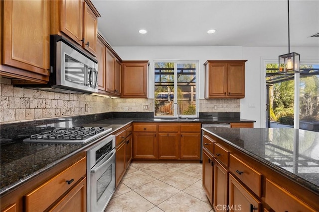 kitchen with backsplash, dark stone counters, stainless steel appliances, sink, and pendant lighting