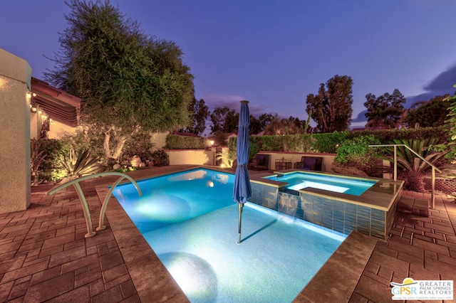 pool at dusk with pool water feature, an in ground hot tub, and a patio