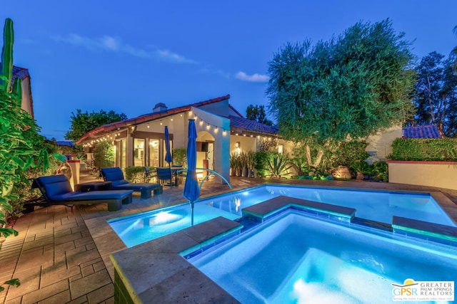 pool at dusk featuring an in ground hot tub and a patio