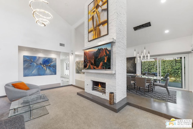 living room with carpet, an inviting chandelier, high vaulted ceiling, and a stone fireplace