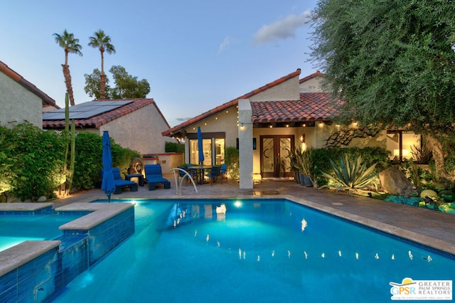 pool at dusk with a patio area and french doors