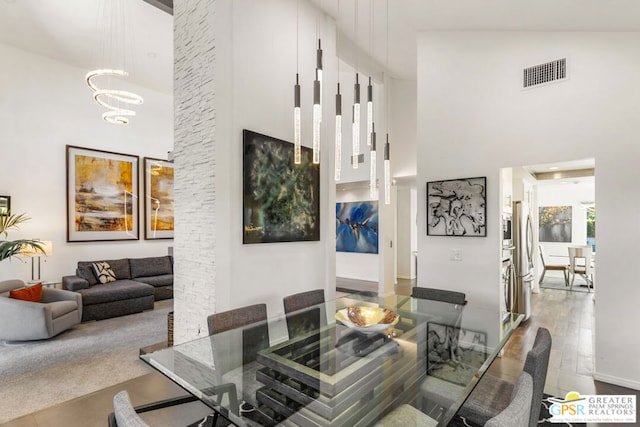 dining area with high vaulted ceiling, wood-type flooring, and a notable chandelier