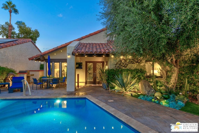 pool at dusk with a patio area and french doors