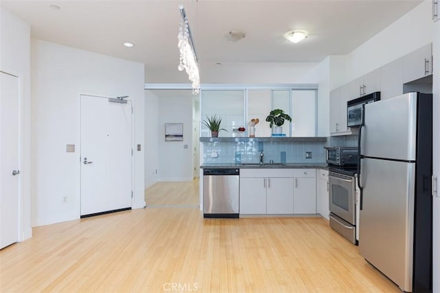 kitchen featuring appliances with stainless steel finishes, backsplash, sink, light hardwood / wood-style flooring, and white cabinets