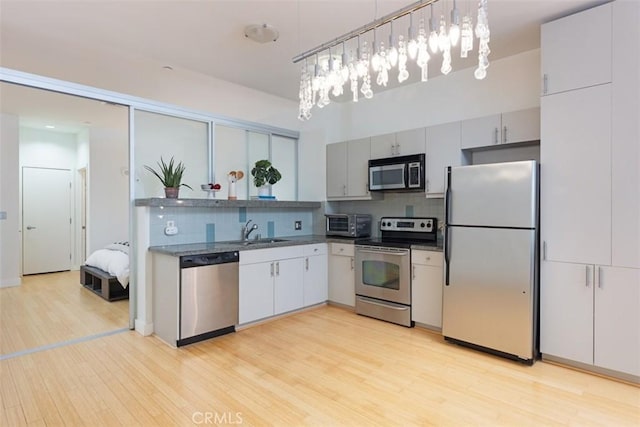 kitchen with backsplash, sink, light hardwood / wood-style flooring, decorative light fixtures, and stainless steel appliances