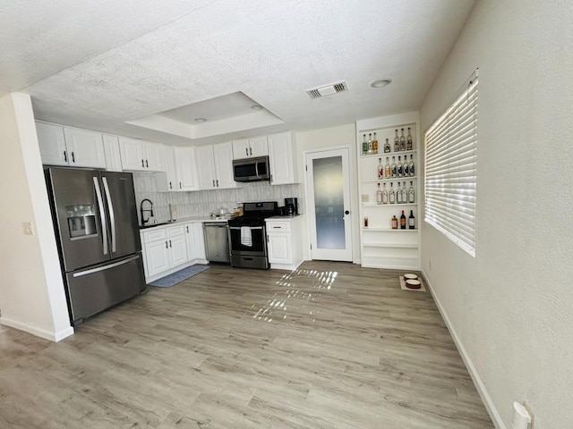 kitchen featuring light hardwood / wood-style flooring, backsplash, a tray ceiling, white cabinets, and appliances with stainless steel finishes