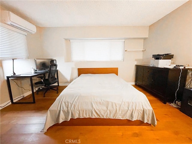 bedroom featuring hardwood / wood-style floors, a textured ceiling, and a wall mounted AC