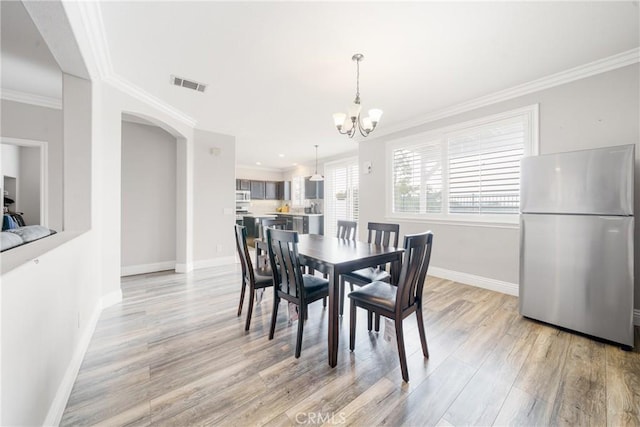 dining space with an inviting chandelier, crown molding, and light hardwood / wood-style flooring